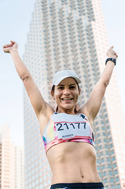 Hispanic Mature Runner Hispanic Mature female Runner smiling with her arms up after finishing an urban marathon miami marathon stock pictures, royalty-free photos & images