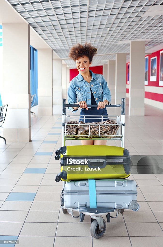Happy tourist at the airport Portrait of teenaged girl pushing an luggage trolley with her suitcases at the airport and laughing at the camera. Airport Stock Photo