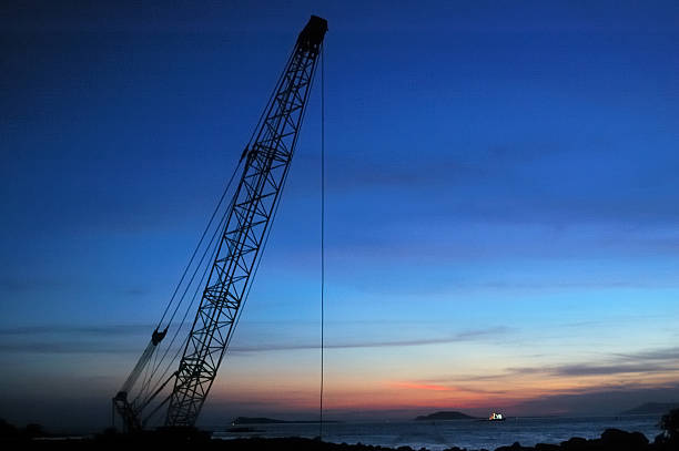 Silhouettes of construction cranes against the backdrop of an orange sunset sky, a photo taken from street level with buildings and wires in the foreground.