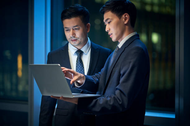 two asian businessmen discussing business in office using laptop computer stock photo