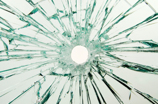 A safety glass car window with a bullet hole through the glass. Close-up. The hole is rough because of the plastic in the glass layers.