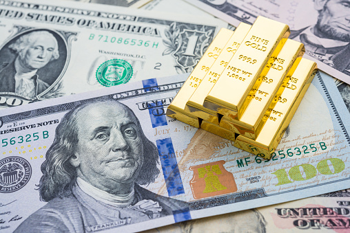 Gold bars on US dollar bill banknotes background. Concept of gold future trading, online asset commodity trading or buy gold bars for investment. It has been valued as a global currency, a commodity, an investment.