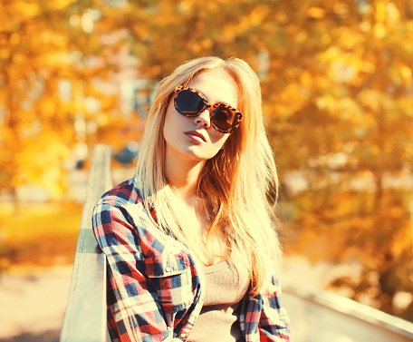 Portrait of beautiful young blonde woman wearing sunglasses in autumn park