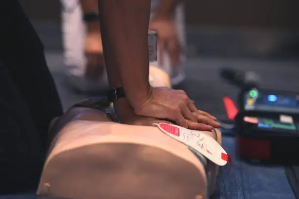 Asian man practicing CPR on a plastic mannequin with Automated External Defibrillator (AED) on the floor. Basic rescue and first aid training.