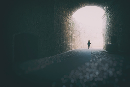 Woman walking into the light inside the high-ceilinged tunnel.