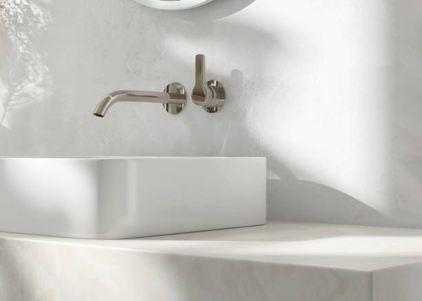istock Cream marble vanity counter top, white modern rectangle ceramic washbasin, chrome faucet, flower vase in bathroom in sunlight and shadow 1602205938