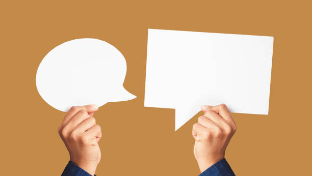 istock Close-up of hands holding white speech bubbles against a light brown background 1602322184