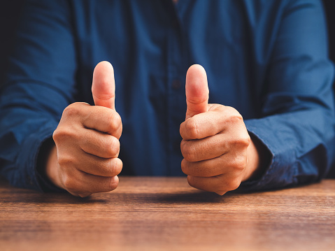 Businessman showing thumbs up with both hands while sitting at the table in the office. Close-up photo