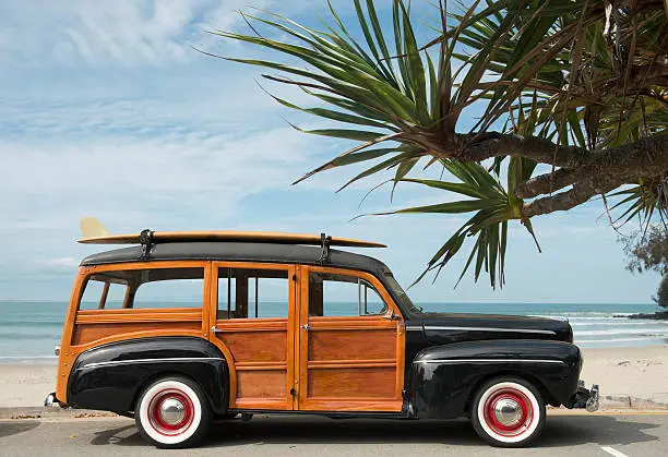 vintage woodie car with surfboard on the roof parked