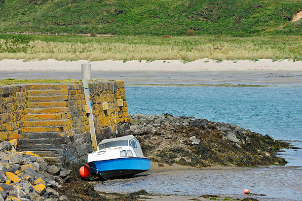 A wide angle view of low tide in Alnmouth beach and harbour in Northumberland. There is a lone sailboat on the hard sand and the weather is overcast.