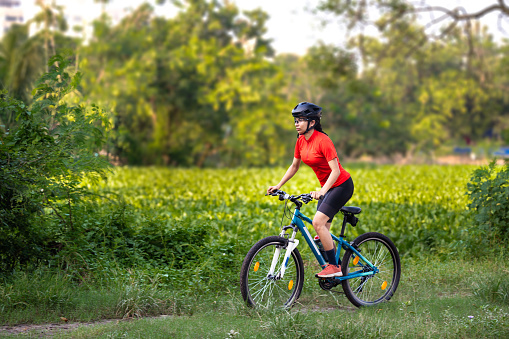 Outdoor image of Young professional woman cyclist enjoy the beautiful ride on her mountain bike in summer forest trail. She is wearing sportswear, hand gloves and helmet while riding.