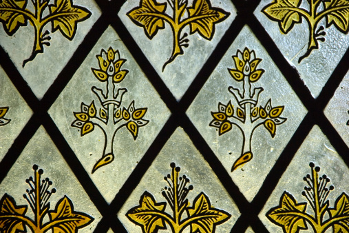 Leaded stained glass window depicting gold coloured leaves and branches with a crown. In a church in the village of Ilam, Derbyshire.