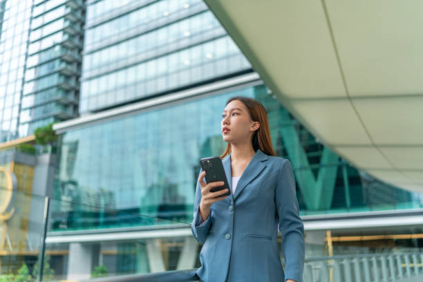 istock Business on the Move. Connected Mobility. Young asian businesswoman using her smartphone while commuting to her work place in a central business district against the backdrop of corporate buildings 1602472761