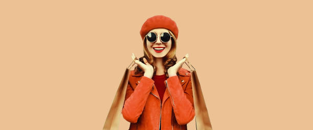 Autumn portrait of beautiful happy smiling young woman with shopping bags wearing red jacket, beret on brown background stock photo