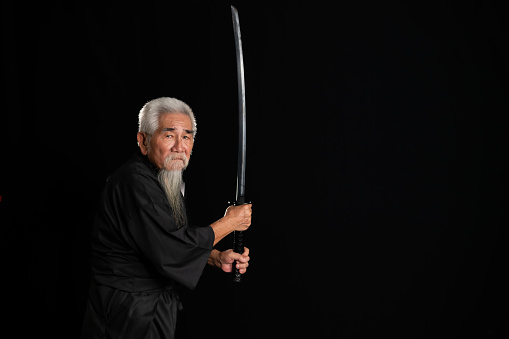 Senior Japanese samurai with katana sword on black background, studio shot