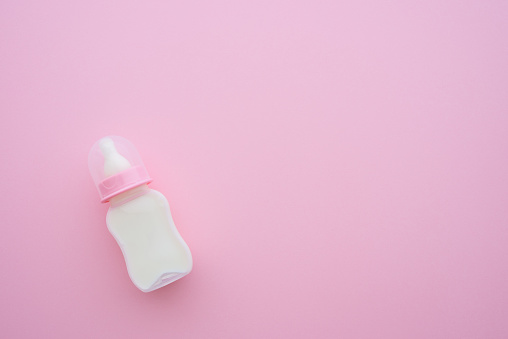 Top view of baby toddler feeding plastic bottle and soft teat with milk on pink background with copy space. Newborn accessories prepare for baby girl or toddler from day one, breastfeeding concept.