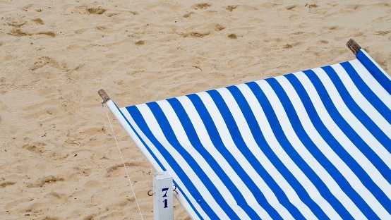 An umbrella with white and blue striped fabric on a sandy beach
