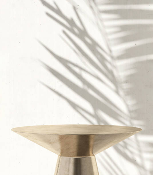 istock Gold shiny round steel pedestal side table podium in sunlight, palm tree leaf shadow on white cement wall 1602512679