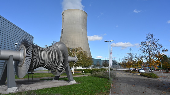 Däniken, Switzerland 10 22 2021: Low-pressure turbine rotor with shrouded and standing blades used in Gösgen nuclear power plant exhibited in front of main building. Behind is huge cooling tower.