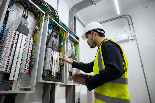 Electrical Engineer team working front control panel, An electrical engineer is installing and using a tablet to monitor the operation of an electrical control panel in a factory service room.