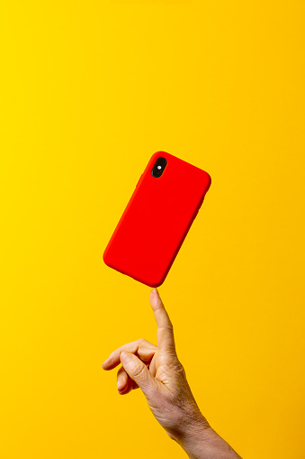 Woman's hand holding a red smartphone with one finger, against a yellow background.