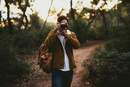 Young man taking a picture with a digital camera and hiking in a forest