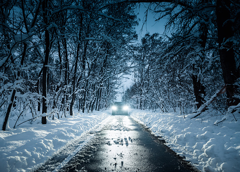 Symmetric shot in cold tones of front of a car on narrow snow covered road thorough a deciduous forest.