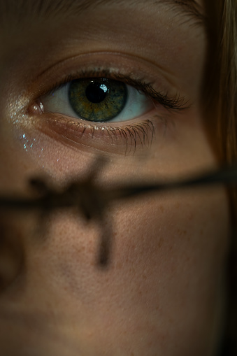 Close up of human eye behind barbed wire