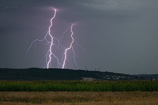 Two branched lightning bolts side by side, striking the earth behind a hilltop in Transylvania, Romania.