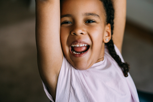 A close up view of a smiling adorable Cuban child looking at camera with her arms raised.