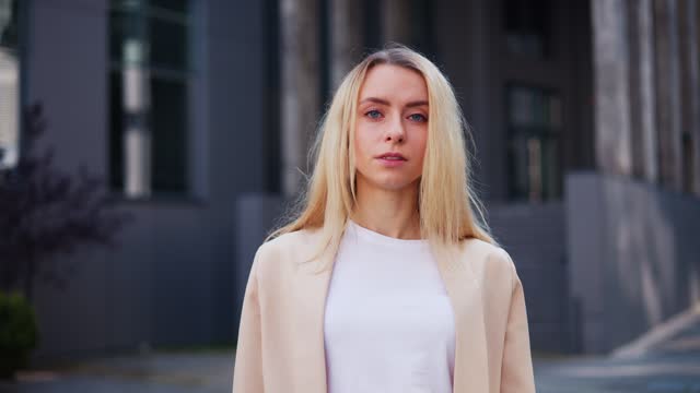 Attractive serious pensive successful beautiful executive businesswoman looking at camera, standing near modern office workplace. Young thoughtful female lady posing for business headshot outdoor.