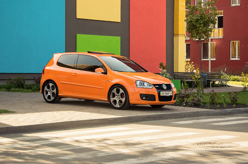 Kyiv, Ukraine - April 26 2014: orange VW Golf GTI in front of colorful building on a sunny day. Three quarter side view of bright Volkswagen hatchback.