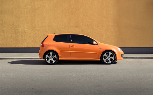 Kyiv, Ukraine - April 26 2014: orange VW Golf GTI in front of orange wall on a sunny day. Side profile view of bright Volkswagen hatchback.