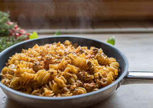 Delicious homemade american comfort food with with fresh creamy beef, pasta and cheese. Served ready to eat in a hot and steaming frying pan on kitchen counter background. Closeup, front view