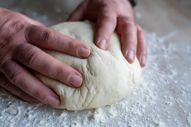 Mens hands kneading a fresh yeast dough on floured kitchen counter