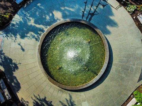 An aerial top view of a water fountain in a green park on a sunny day
