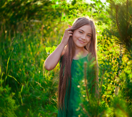 Portrait of a beautiful little girl with long hair in a green dress in the sun
