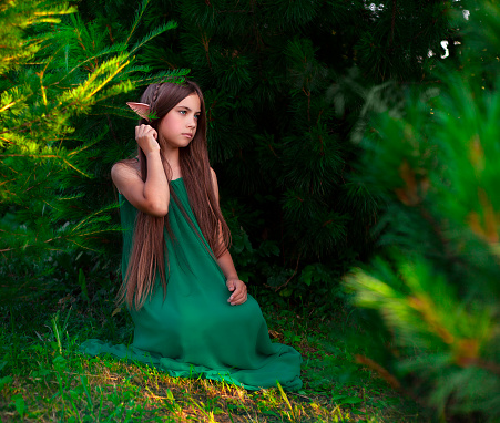 beautiful girl elf sits in a green dress in the forest