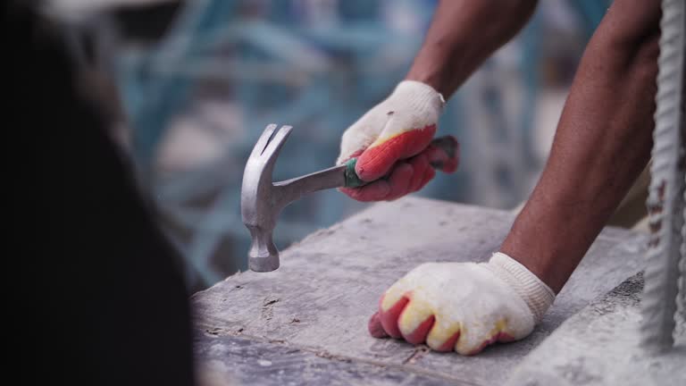 A builder hammers a nail with a hammer