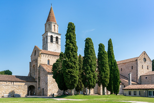 Side view of Basilica di Santa Maria Assunta in Aquileia, Friulli Venezia Giulia, dating back to 4th century, with cypress trees on clear sky summer day