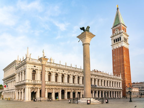 Famous renaissance facade of Library of Saint Mark with Campanile in background and Column with Venetian Lion in foreground on early summer morning