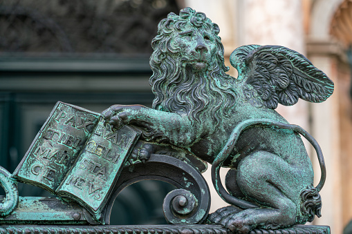 19th century bronze statue of winged St. Mark's Lion holding bible in front of entrance to Campanile on Saint Mark Square