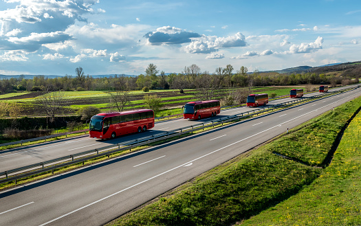 Series of modern red modern buses traveling on a wide highway in a rural backdrop. Convoy of buses. Highway transportation of passengers in a bus line.