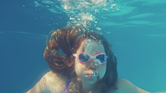 Young Caucasian Girl Diving in Swimming Pool Breathing Out Air Bubbles