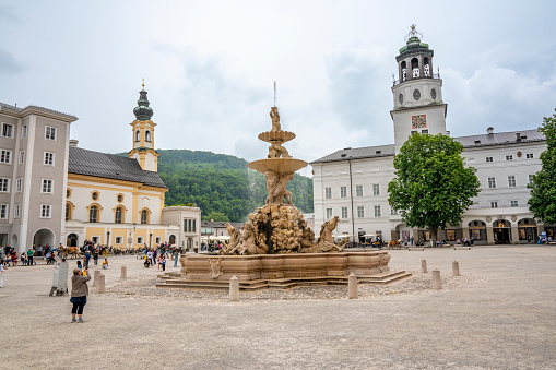 Residenzplatz square with Residenz fountain in the Old Town of Salzburg, Austria during an overcast springtime day with tourist walking on the square.