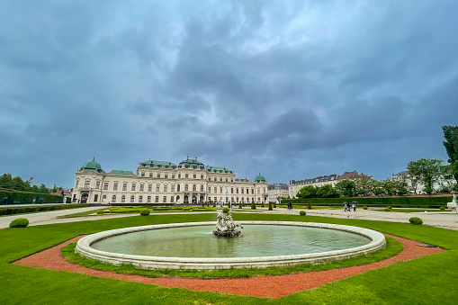 Belvedere Baroque palace in Vienna seen from the public gardens with fountains and dark clouds above.