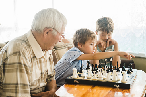 An elderly gray-haired man teaches boys to play chess