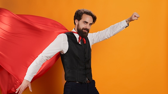 Confident waiter with red hero cape posing as a superhero on camera, determined to serve clients. Superhuman restaurant employee serving food and drinks, hero character costume with mantle.