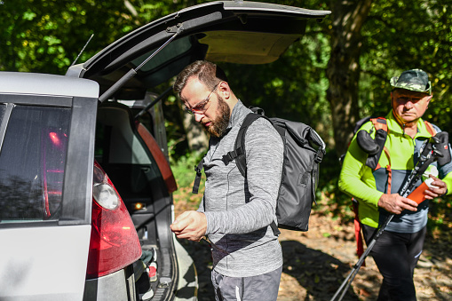 Hikers Of Different Ages Picking Up Equipment From Car Trunk