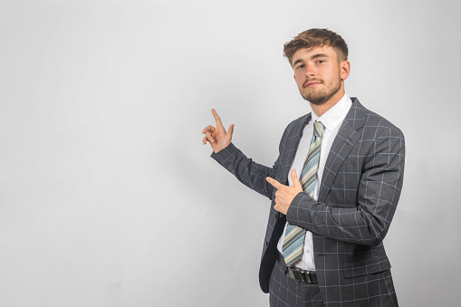 Portrait of a young entrepreneur in a suit and tie pointing to the side against a plain background